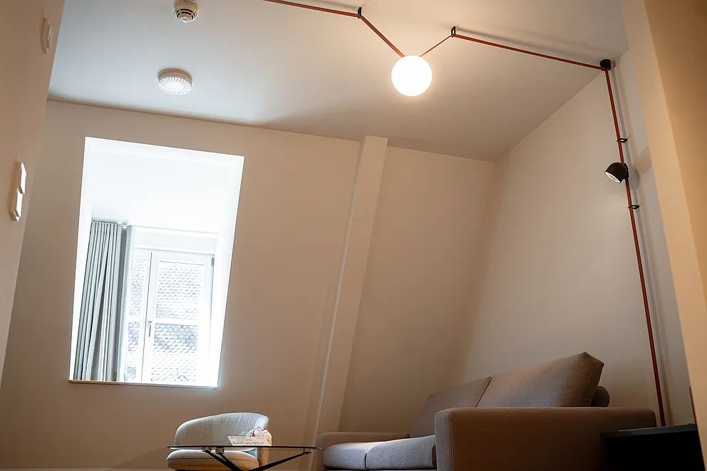 Wohnbereich der Suite im Haus Ehemalige Sparkasse mit Sofa unter der Dachschräge und Kugelleuchte an kupferfarbenem Gestänge