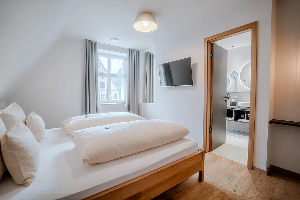 Schlafzimmer der Suite im Haus Ehemalige Sparkasse mit Doppelbett, Wand-TV und offener Tür zum Bad