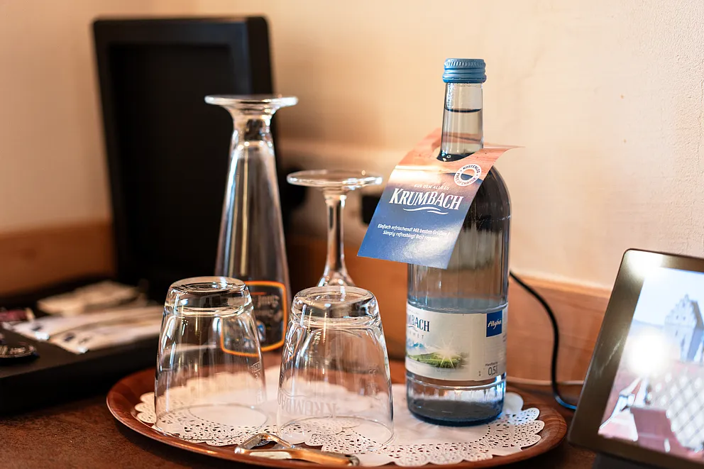 Vier Gläser und eine Mineralwasserflasche mit Anhänger auf einem runden Tablett mit Spitzendeckchen