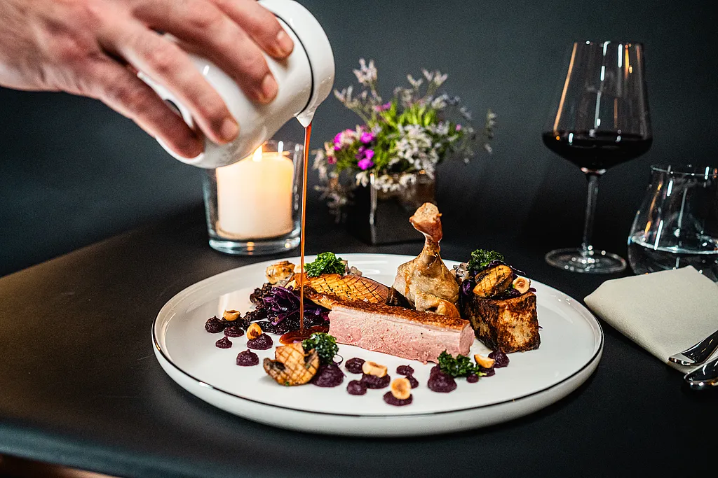 Rosa gebratene Entenbrust mit Keule, Rotkohl und Haselnüssen, Soße wird aus einem weißen Kännchen angegossen