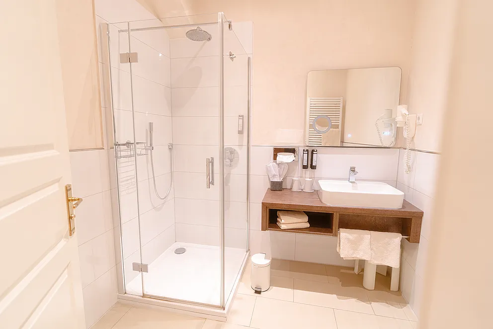 Bad im Superior-Zimmer des Stammhauses mit Glasdusche und Regenbrause, Aufsatzwaschbecken auf Holzablage und Spiegel