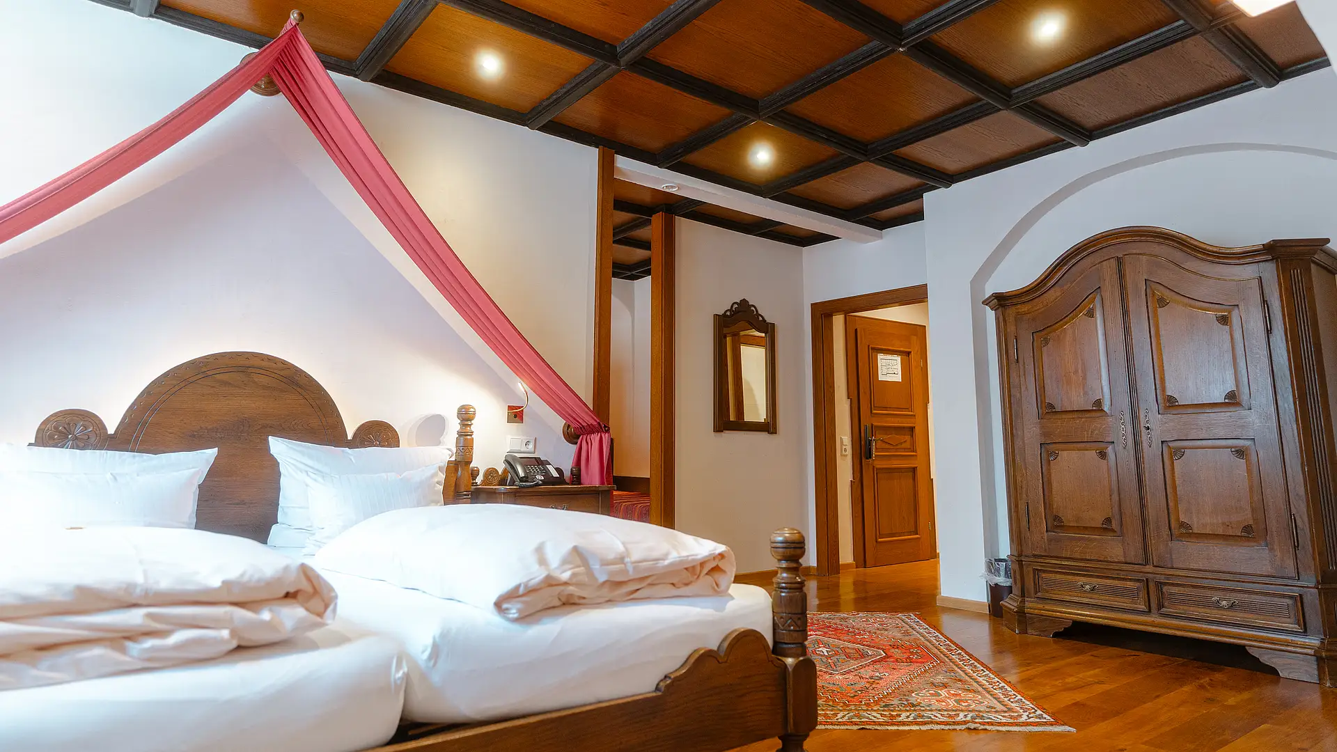 Herrensuite im Stammhaus mit Himmelbett unter rotem Stoffbaldachin, geschnitztem Holzschrank und Holzkassettendecke