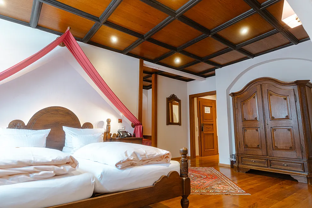 Herrensuite im Stammhaus mit Himmelbett unter rotem Stoffbaldachin, geschnitztem Holzschrank und Holzkassettendecke