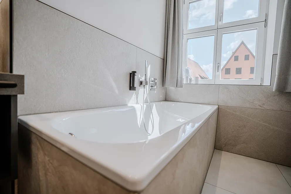 Badewanne am Fenster im Bad der Suite im Haus Ehemalige Sparkasse mit Blick auf ein rosafarbenes Giebelhaus