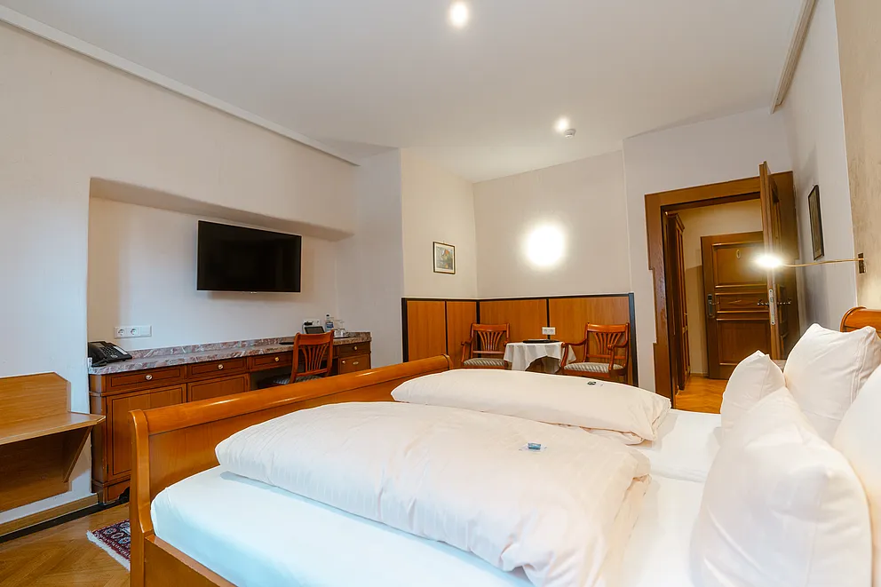 Komfortzimmer im Stammhaus mit Doppelbett, Fernseher in einer Wandnische über der Holzkommode und kleiner Sitzecke