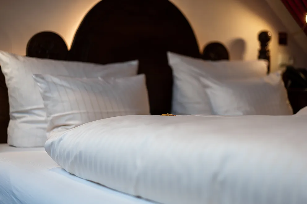 Bett mit weißer Bettwäsche vor dunklem Holzkopfteil in der Herrensuite im Stammhaus