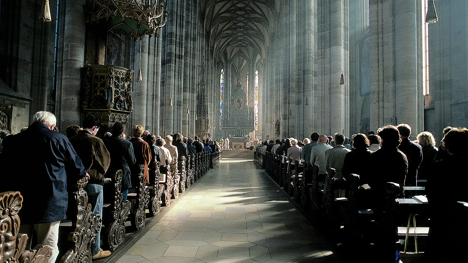 Innenraum des Münsters St. Georg mit schlanken Pfeilern, Netzgewölbe und Kanzel, in den Bänken zahlreiche Besucher