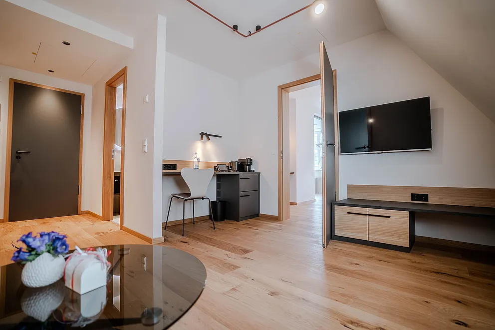 Wohnbereich der Suite im Haus Ehemalige Sparkasse mit Glastisch und Blumen, Schreibtisch und Wand-TV