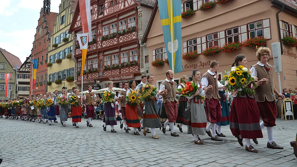 Jugendliche in historischen Gewändern mit Sonnenblumensträußen beim Festzug, dahinter Fachwerkhäuser mit Blumenkästen