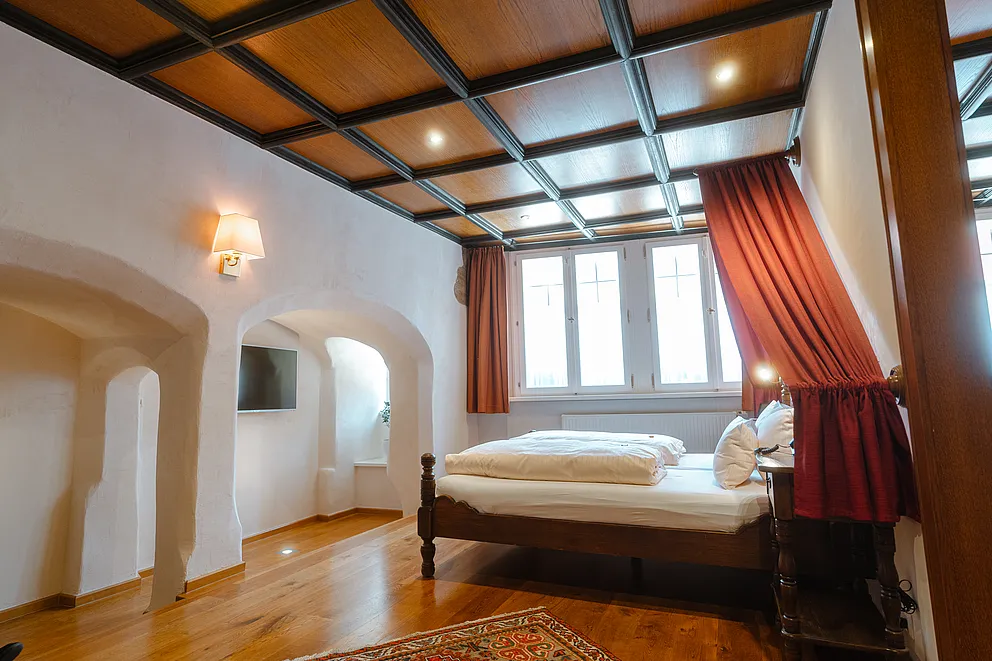 Schlafzimmer der Herrensuite im Stammhaus mit Himmelbett, roten Vorhängen, Holzkassettendecke und Rundbogennischen