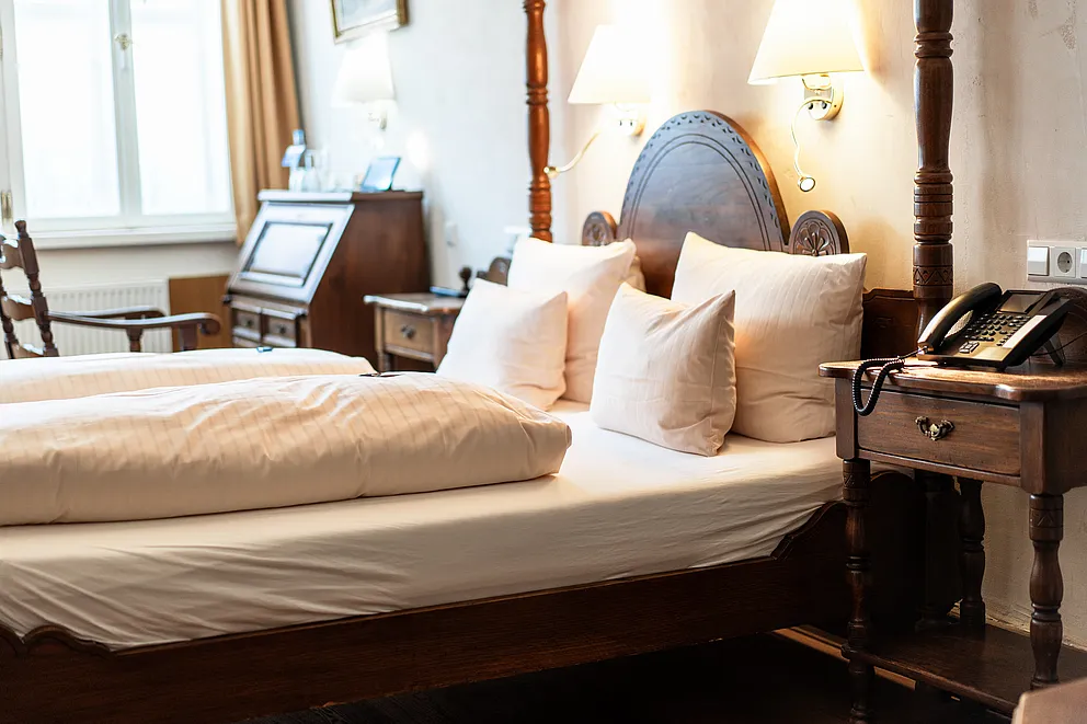 Himmelbett aus dunklem Holz mit geschwungenem Kopfteil, Wandleuchten und Nachttisch mit Telefon in der Hochzeitssuite