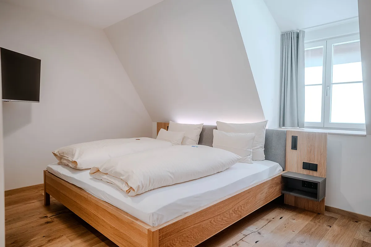 Zimmer im Haus Ehemalige Sparkasse mit Doppelbett aus Holz unter der Dachschräge, Wandfernseher und Holzdielenboden