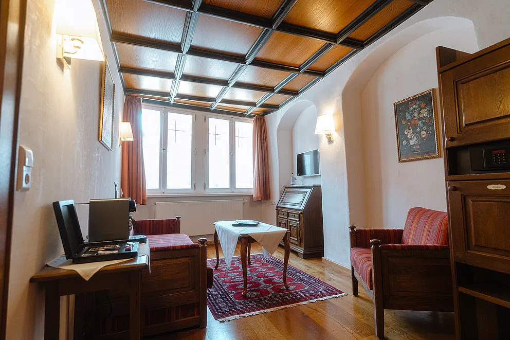Wohnzimmer der Herrensuite im Stammhaus mit Orientteppich, Tisch mit weißer Decke, Sekretär und rot gestreiften Sesseln