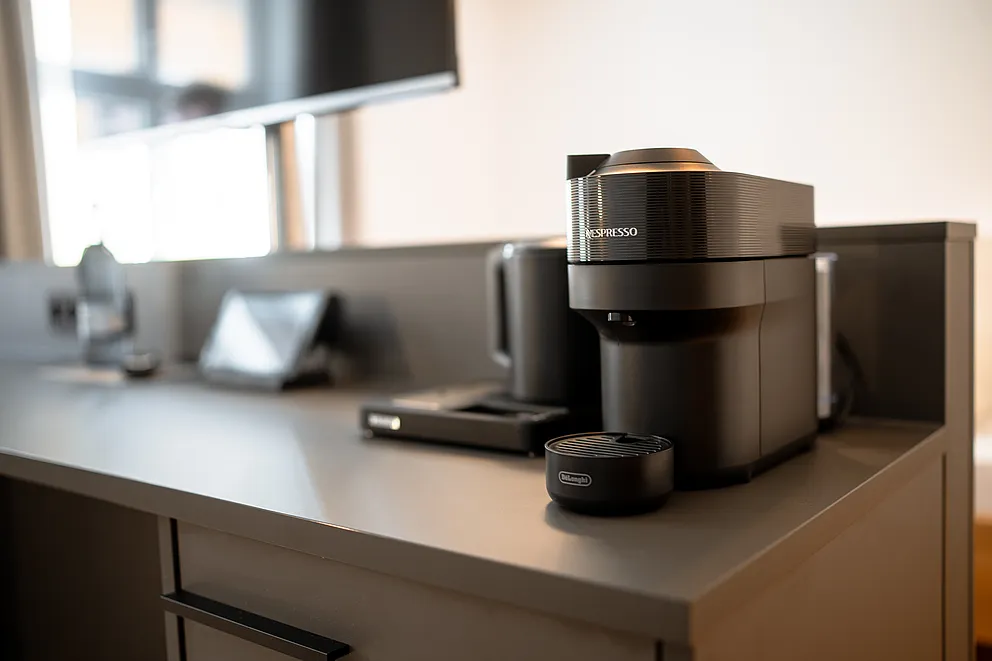 Nespresso-Kaffeemaschine und Wasserkocher auf einem grauen Schreibtisch am Fenster