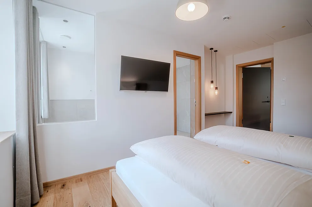 Blick vom Bett auf Wand-TV und offene Türen im Schlafzimmer der Suite im Haus Ehemalige Sparkasse