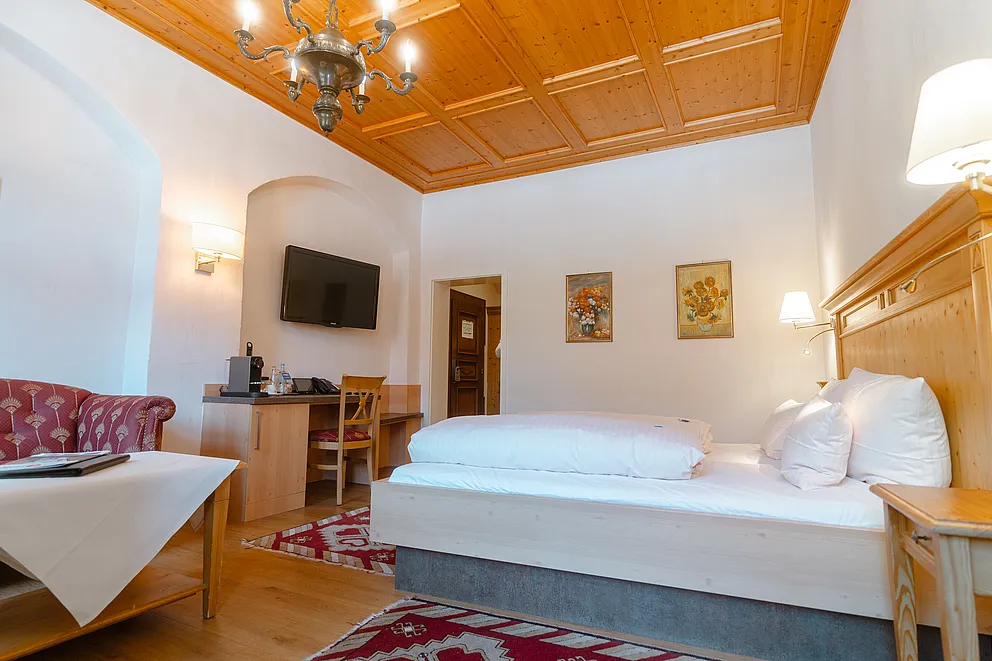 Superior-Zimmer im Stammhaus mit Holzkassettendecke, Kronleuchter, Doppelbett, Schreibtisch in einer Wandnische und Sitzecke