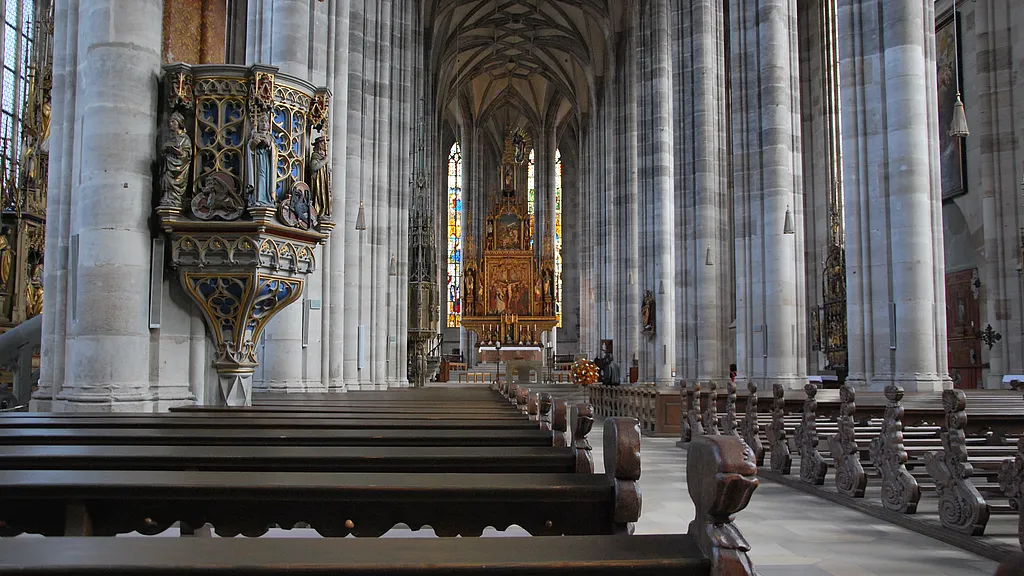 Innenraum des Münsters St. Georg mit verzierter Kanzel am Pfeiler, leeren Kirchenbänken und Blick zum Hochaltar