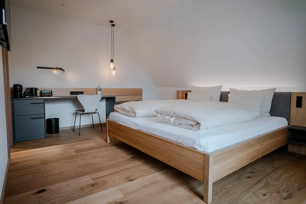 Zimmer unter Dachschräge mit Holzdoppelbett, Hängeleuchten und Schreibtisch mit Kaffeemaschine und Wasserkocher