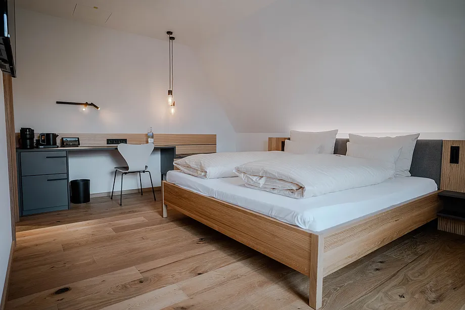 Zimmer unter Dachschräge mit Holzdoppelbett, Hängeleuchten und Schreibtisch mit Kaffeemaschine und Wasserkocher