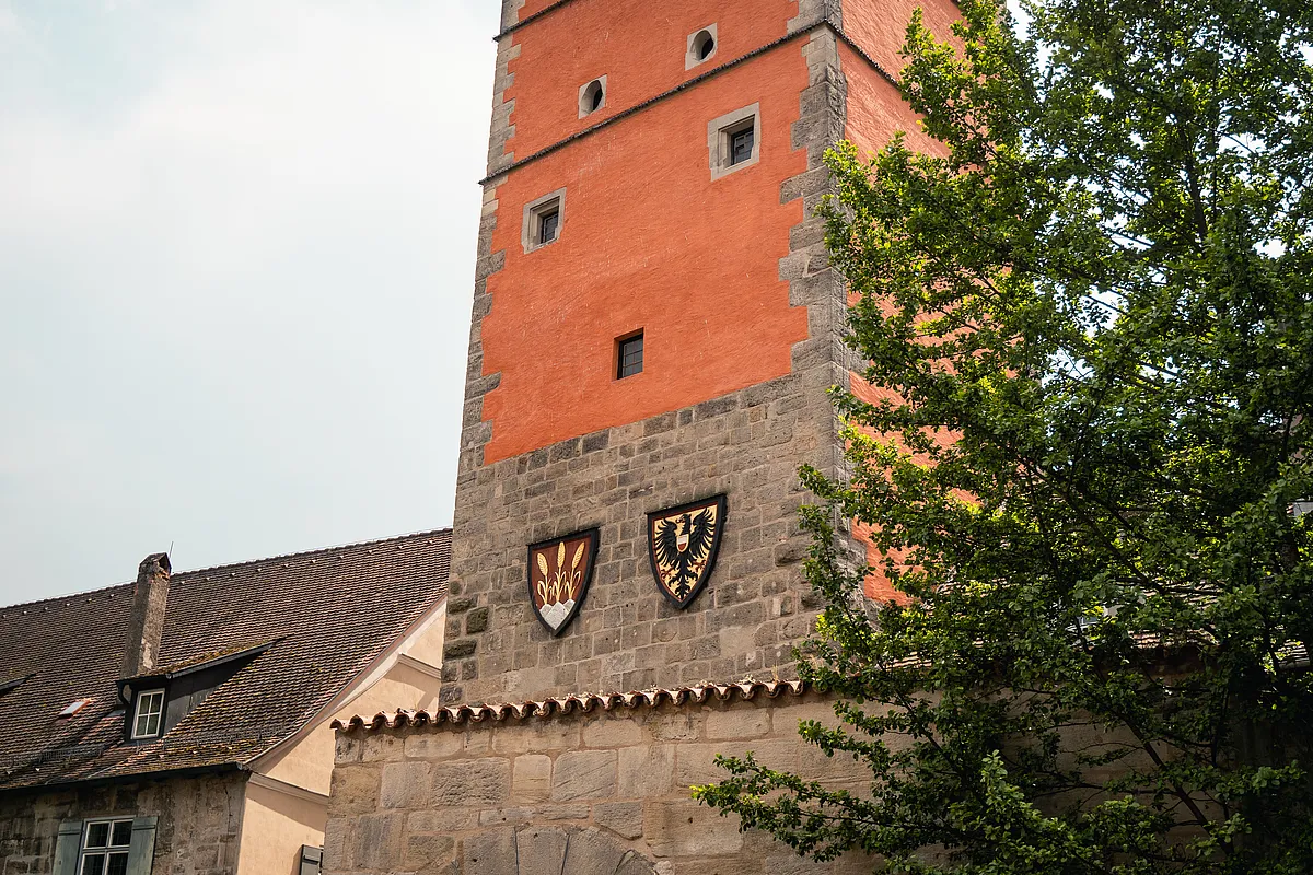 Turm mit Natursteinsockel und rot verputztem Oberbau, daran das Dinkelsbühler Stadtwappen mit Ähren und der Reichsadler