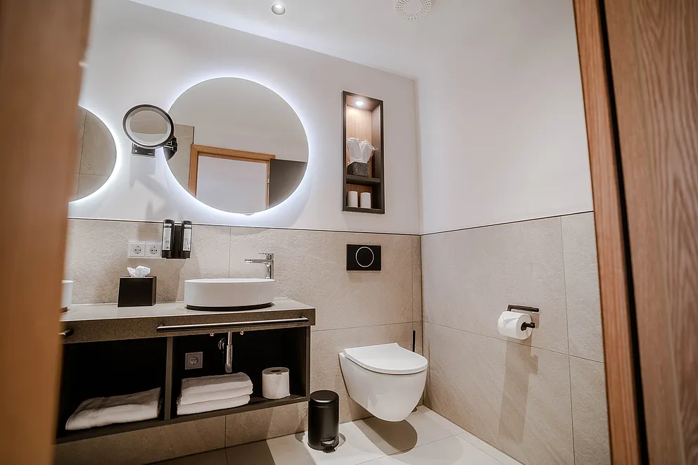 Blick durch die Tür ins Bad des Superior-Plus-Zimmers mit Waschtisch, runden Leuchtspiegeln und Hänge-WC