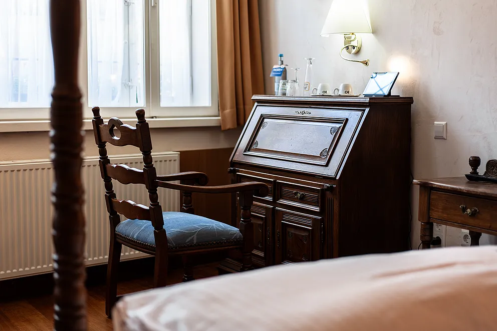 Sekretär aus dunklem Holz und Stuhl mit blauem Sitzpolster am Fenster der Hochzeitssuite, vorn ein Pfosten des Himmelbetts