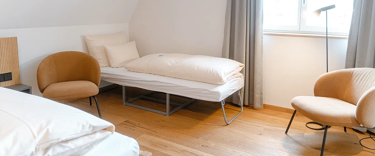Zustellbett zwischen zwei Sesseln unter der Dachschräge im Superior-Plus-Zimmer im Haus Ehemalige Sparkasse