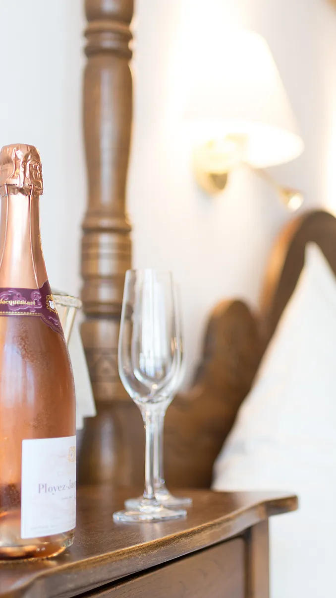 Flasche Rosé-Champagner und leeres Sektglas auf dem Nachttisch eines Zimmers im Stammhaus, dahinter ein gedrechselter Bettpfosten