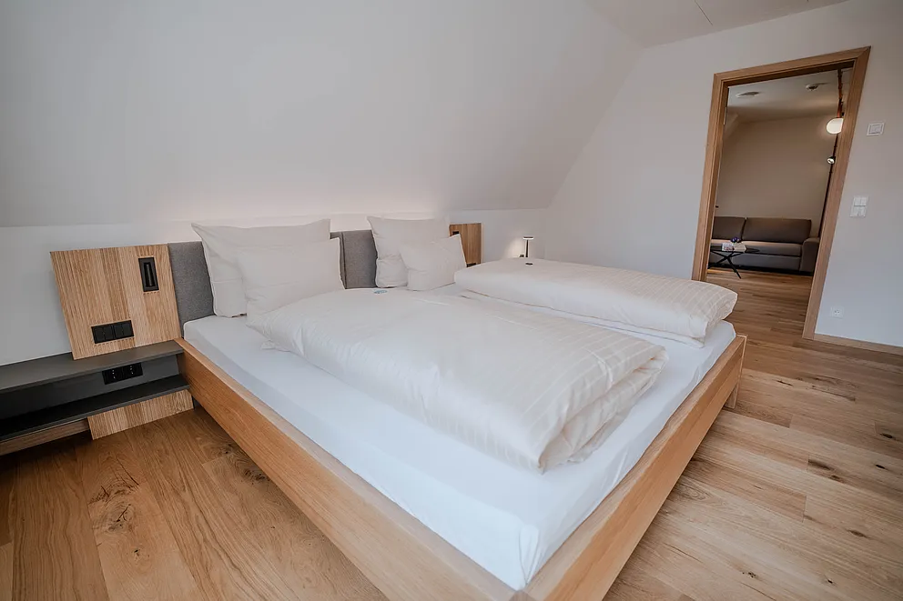 Schlafzimmer der Suite im Haus Ehemalige Sparkasse mit Doppelbett unter der Dachschräge und Blick ins Wohnzimmer