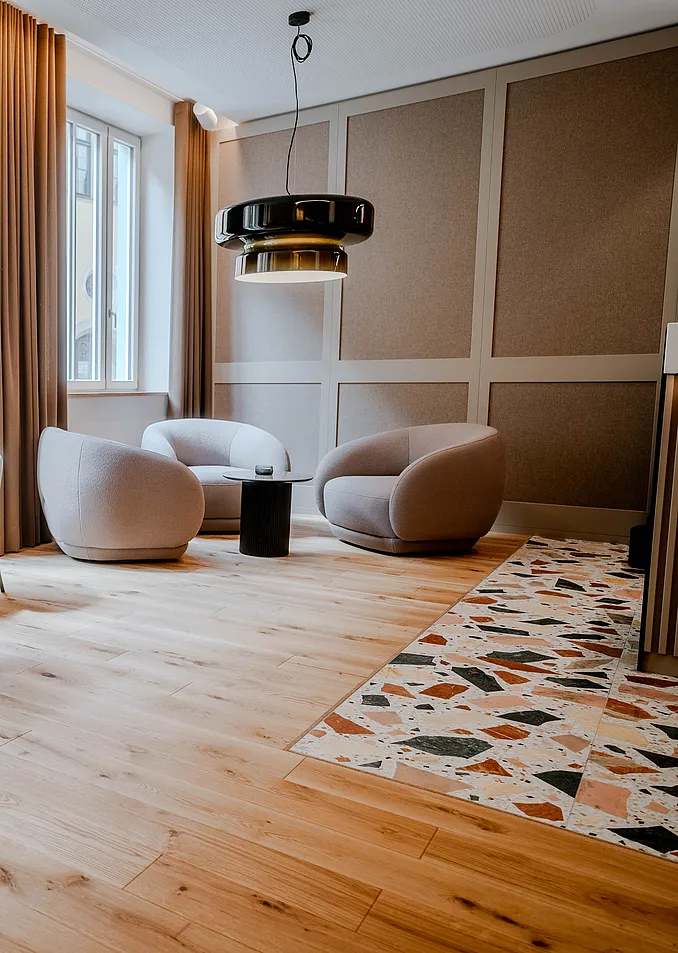 Lounge in der Ehemaligen Sparkasse mit drei runden hellen Sesseln, schwarzer Pendelleuchte und Terrazzo-Einlage im Holzboden