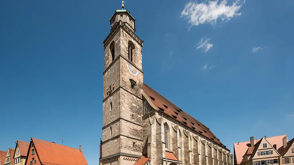 Münster St. Georg mit hohem Steinturm und steilem Ziegeldach vor blauem Himmel, am Rand Giebel benachbarter Häuser