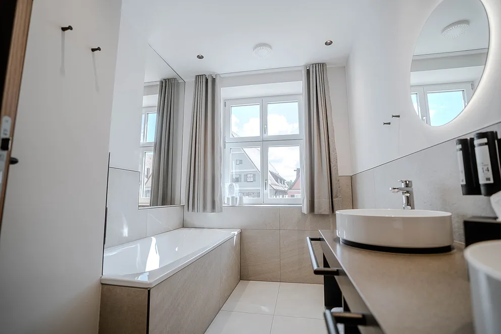 Bad der Suite im Haus Ehemalige Sparkasse mit Badewanne vor dem Fenster und Aufsatzwaschbecken mit rundem Spiegel